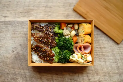 A delicious Japanese convenience store bento box filled with rice, teriyaki beef, broccoli, tamagoyaki, ham, and salad.