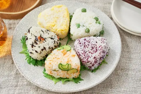 A colorful assortment of musubi vs onigiri, each a unique rice ball shape with various toppings like peas, seaweed, and cucumber.