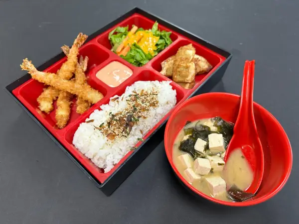 A delicious shrimp bento box with crispy fried shrimp, rice, salad, and tofu, served with miso soup.