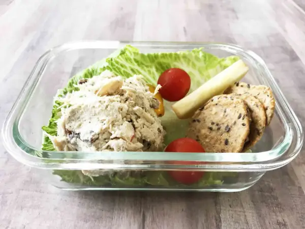 A delicious chicken salad bento box with lettuce, cherry tomatoes, a pickle spear, and crackers.
